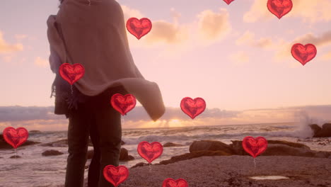 multiple heart balloons floating against young couple embracing each other near sea shore