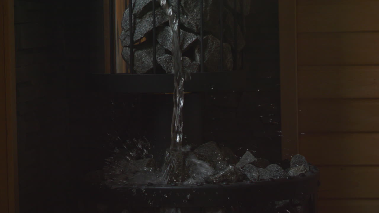 Water poured on sauna hot stones producing steam, slow motion