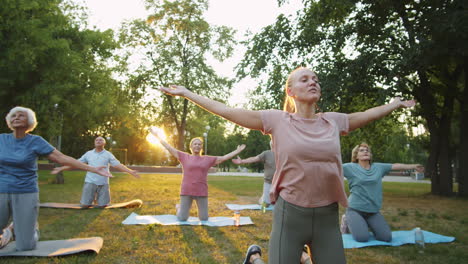 female instructor leading outdoor yoga class with senior people