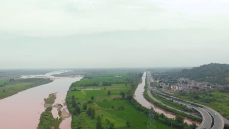 Vista-Aérea-Del-Paso-Elevado-Sobre-Tierras-Agrícolas-Cerca-Del-Río,-Y-El-Canal-Después-De-La-Lluvia-Con-Agua-Turbia-Lluviosa-Fuera-De-La-Ciudad-En-La-Región-De-Punjab,-India