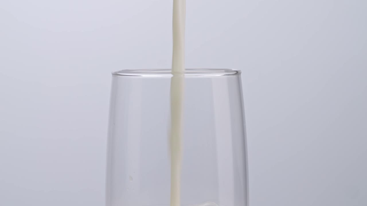 Close Up Of Milk Being Poured Into Drinking Glass On White Background