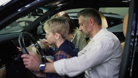 A-middle-aged-man-with-gray-hair-in-a-white-shirt-along-with-his-wife-and-little-blond-son-with-blue-eyes-are-sitting-in-the-interior-of-a-modern-car-during-their-trip-to-a-car-dealership