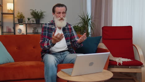 anciano mirando una computadora portátil, haciendo una llamada de conferencia de videocámara con amigos o familiares en casa
