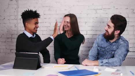 Multi-ethnic-business-team-giving-high-five-sitting-at-the-table-in-modern-office.-Slow-Motion-shot