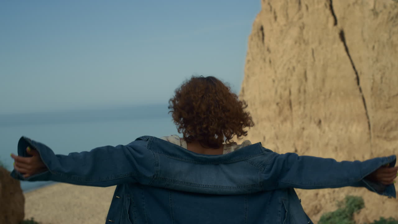mujer joven bajando por la costa a la playa vista de atrás. niña extendiendo los brazos.