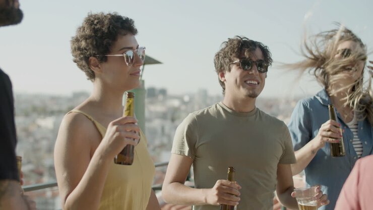 Happy friends drinking beer and dancing at rooftop party on a summer day
