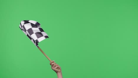 female hand holding and waving checkered race flag in slow motion against green screen background. victory, achievement, success, sport concept. silk black and white checkered flag finish start race