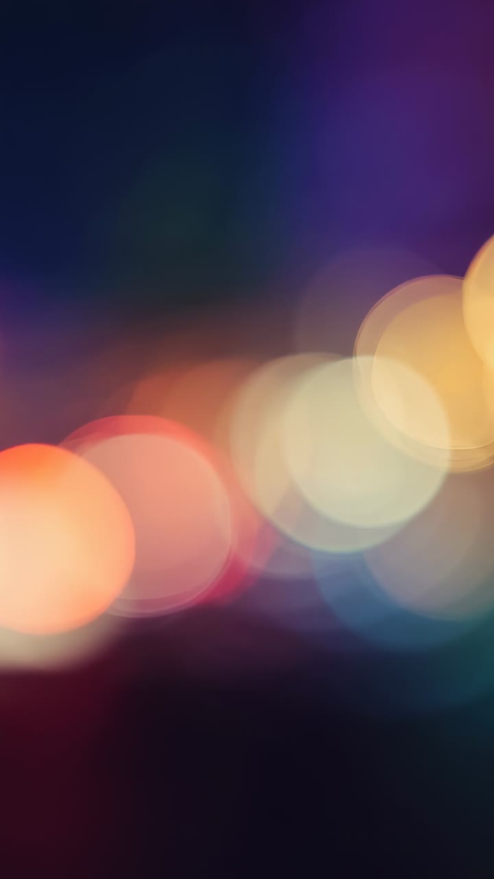 Vertical video: Bokeh circles drifting in defocused scene after playback start, with rainbow glow