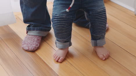 Pies-De-Cerca-Madre-Enseñando-Al-Bebé-A-Caminar-Niño-Dando-Los-Primeros-Pasos-Con-Mamá-Ayudando-Al-Bebé-Sosteniendo-Al-Niño-Apoyando-El-Equilibrio-En-Casa