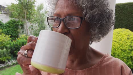 primer plano de una mujer afroamericana mayor que usa un teléfono inteligente mientras bebe café sentada en el cerdo