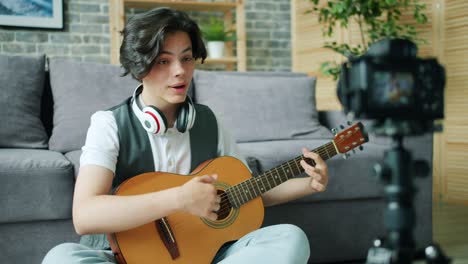 teenage musician recording video holding guitar using modern camera in apartment