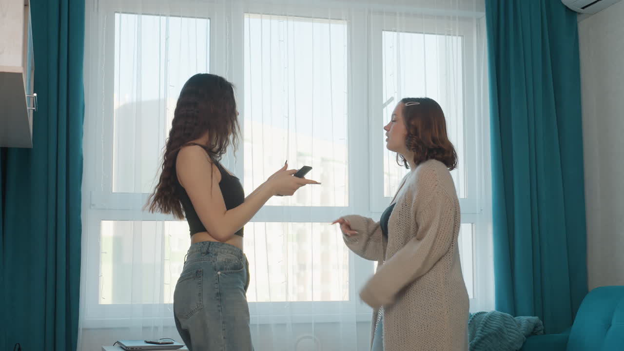 Two White Women Duet Rehearsal By Window Using Smartphone As Mic Cozy Living Room With Teal Curtains Denim And Cardigan Morning Sunlight Playful Laughter Roommate Bonding Performance Practice