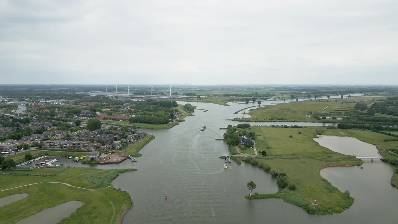 A peaceful aerial view of a river cutting through a flat Dutch landscape with villages and wind turbines in the background.