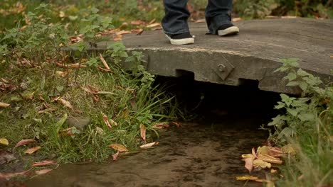 Person-crosses-small-stream-over-wooden-bridge-in-autumn