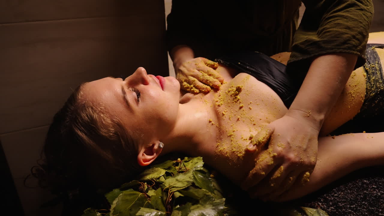 Woman enjoying a spa treatment with a body scrub and herbal leaves