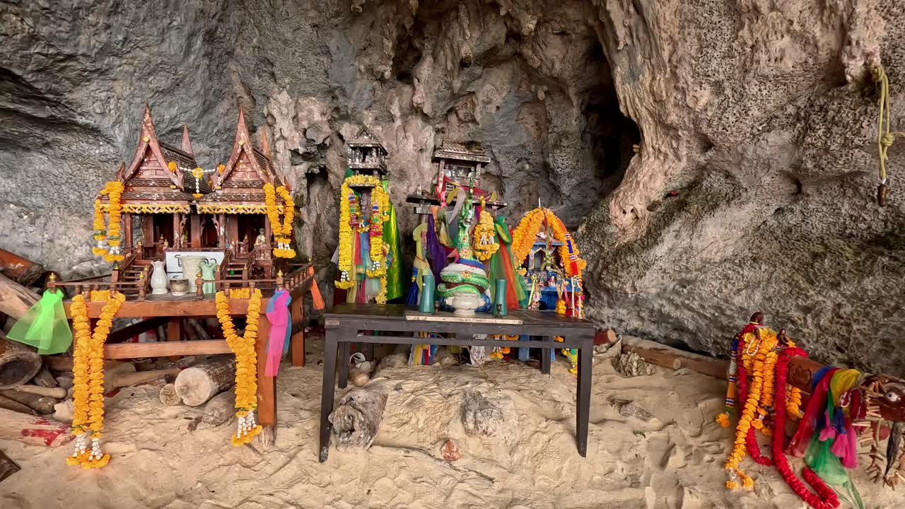 Panning left on a Hindu animist shrine decorated with offerings and phallic symbol called lingams in Phra Nang Cave or Princess Cave, showing the authentic local thai folklore. Krabi, Thailand