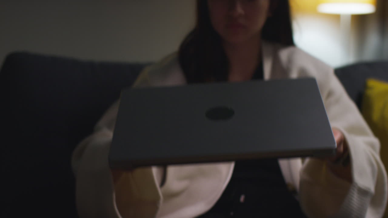 primer plano de una mujer pasando la noche en casa sentada en el sofá y abriendo la computadora portátil para navegar en línea 1