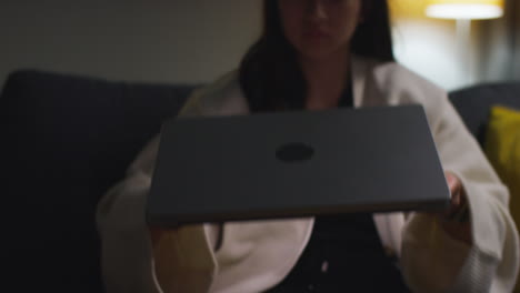 primer plano de una mujer pasando la noche en casa sentada en el sofá y abriendo la computadora portátil para navegar en línea 1