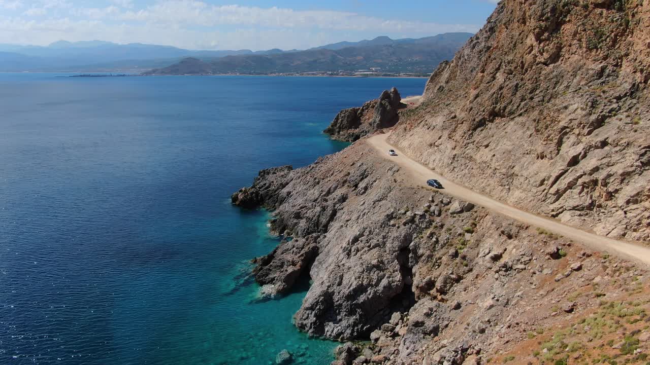 Crete Greece, a stopped car is passed by another near Balos Beach on a seaside cliff road to the beach, Aerial approach shot with blurred plates