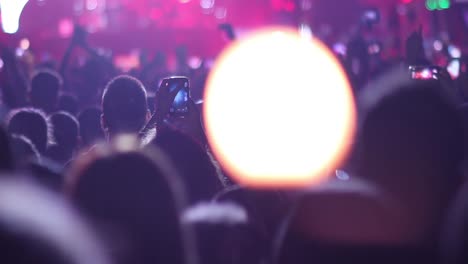 Crowd-attending-a-concert,-people-silhouettes-handling-lights-with-flame-flare-effect-and-raised-hands-in-air-at-music-festival