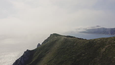 bird's eye view of a breathtaking steep rocky coast line with heavy dense fog approaching from the sea and moving over hill, far east, russia, sea of japan