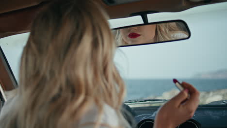 seductive woman applying makeup lips looking in automobile mirror close up.