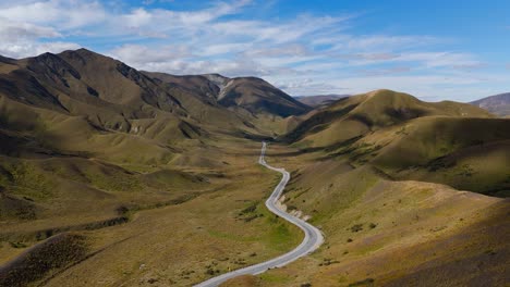 Winding-road-on-valley-floor-and-mountains-across-Lindis-Pass,-aerial