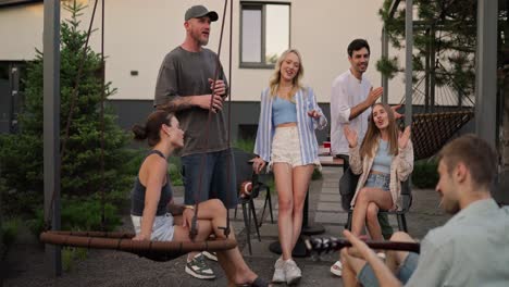 Cheerful-group-of-friends-sing-a-song-while-their-friend-plays-a-cheerful-melody-on-the-guitar-during-a-party-in-the-backyard-of-a-house