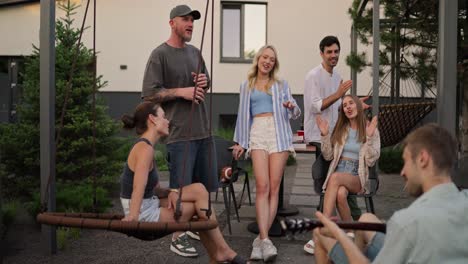 un grupo alegre de amigos canta una canción mientras su amigo toca una melodía alegre en la guitarra durante una fiesta en el patio trasero de una casa