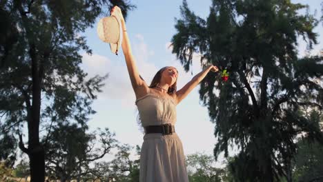 Mujer-Muy-Feliz-Y-Libre-Levantando-Los-Brazos-Con-Sombrero-Y-Rosa-En-La-Naturaleza-Al-Atardecer