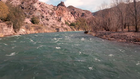 Low-altitude-flight-over-a-river-in-a-canyon,-capturing-the-exhilarating-thrill-and-stunning-beauty-of-the-meandering-watercourse-within-the-rugged-canyon-walls