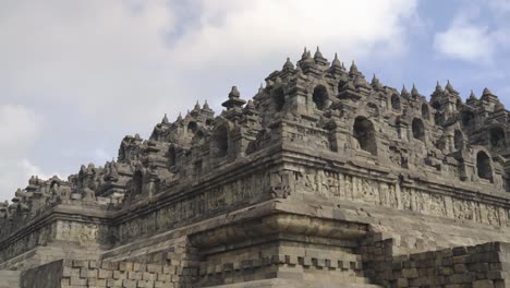 Close-view-on-the-famous-Borobudur-temple-with-its-details-and-black-walls-statues-in-Yogyakarta-Java-Indonesia---panning-shot-on-a-bright-day-with-greeneries