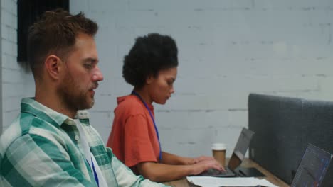 a man and woman work at laptops, sitting at one work desk in a office