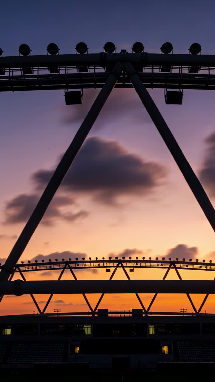 Video verticale: Inquadratura di una grande capriata luminosa ad arco in acciaio che si oscura nello stadio mentre i colori del tramonto cambiano.