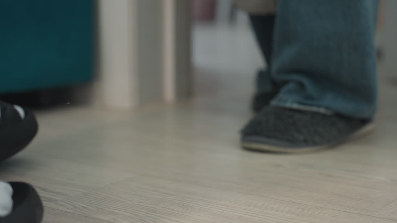 Slippers And Denim Jeans Stepping Over Hardwood Threshold. Closeup At Apartment Entrance With Soft Sole Contact, Casual Student Arrival Vibe, Subtle Shuffle And Quiet Domestic Routine Near Living