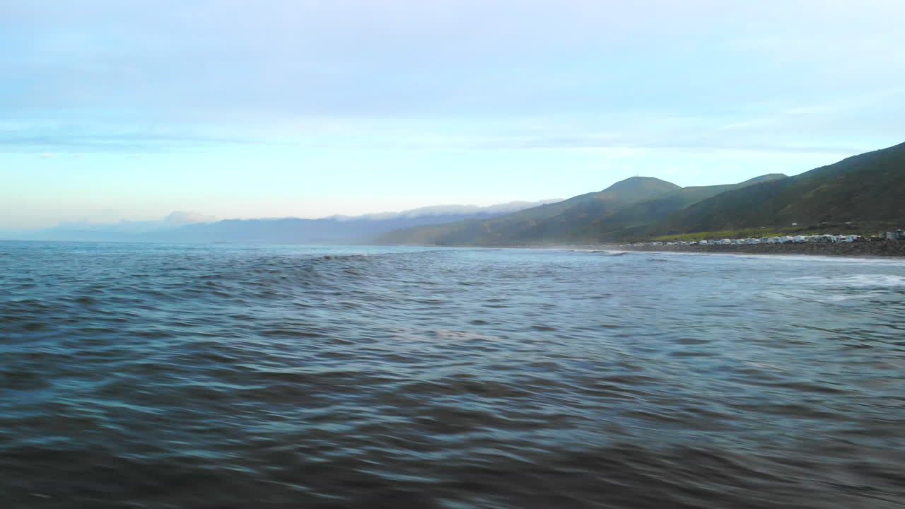 Aerial drone shot flying fast and low over the sea water of the Pacific ocean waves breaking on the Ventura, California coast line at sunrise
