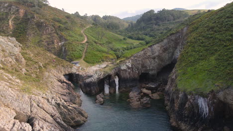 Vista-Aérea-De-La-Hermosa-Costa-Salvaje-Del-Acantilado-Mientras-Un-Grupo-De-Personas-Caminan-Y-Disfrutan-De-Las-Vistas-En-Un-Día-De-Verano