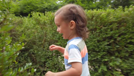 baby boy with long hair running through a hedge maze in slow motion