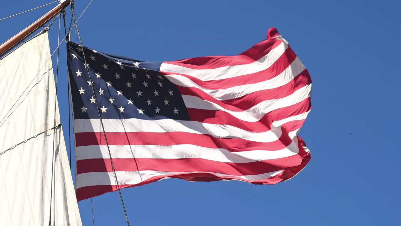 Wind-blown flag of USA with a blue sea in background. Sunny day shot. Close up. Bottom view