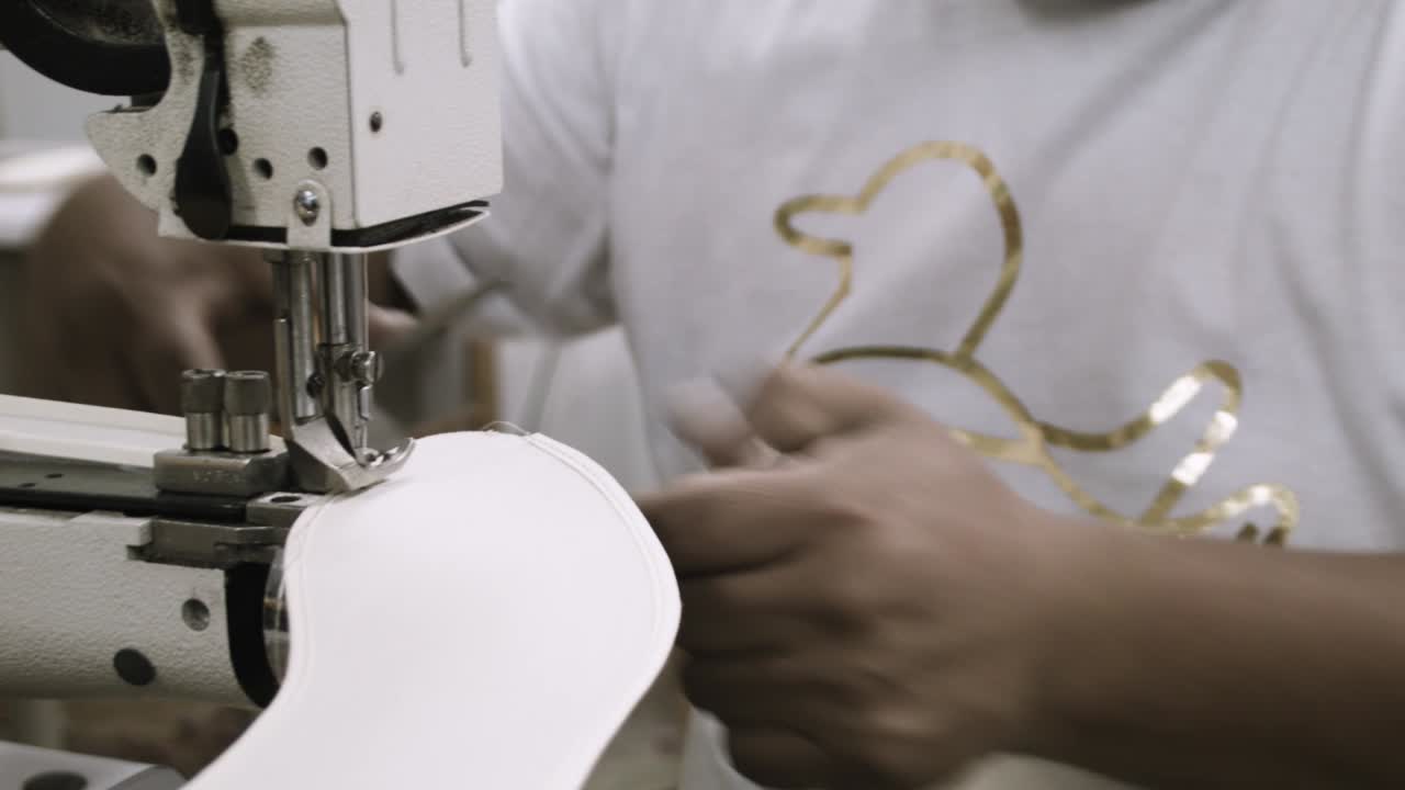 한 남자가 공장 환경에서 직물과 직물을 꿰맨다