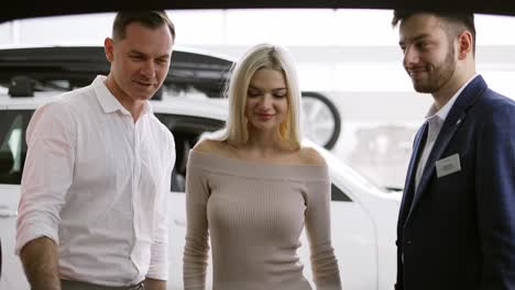 salesman showing the capacity of a trunk from inside to customers in car showroom