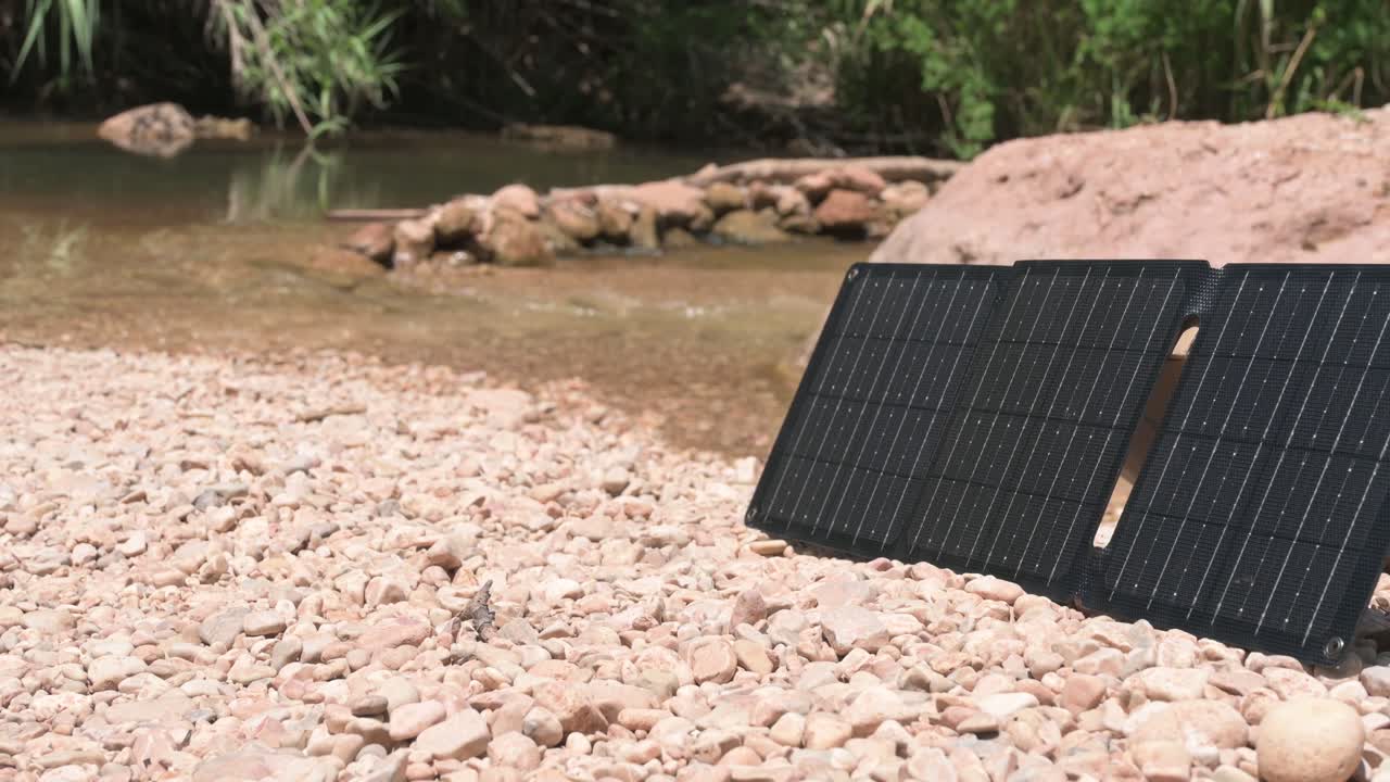 Portable solar panels stand upright on a rocky riverbed, showcasing renewable energy solutions in a natural setting
