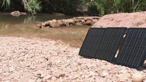 portable solar panels stand upright on a rocky riverbed, showcasing renewable energy solutions in a natural setting