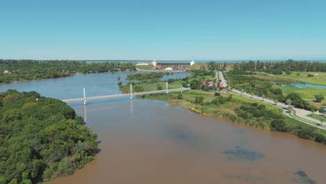 A-stunning-aerial-image-featuring-a-bridge-with-the-Frontal-Dam-of-Río-Hondo-in-the-background,-set-against-the-backdrop-of-a-beautiful-sunny-day