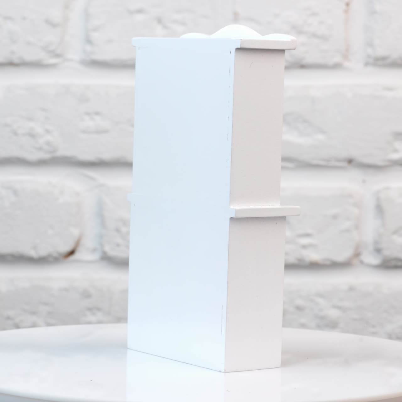 Cute white wooden cupboard rotating on the table. Little toy furniture close up at white backdrop