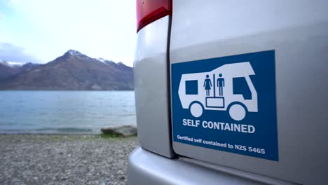 slowmo - self-contained motorhome by beautiful blue lake wakatipu, queenstown, new zealand with mountains fresh snow cloudy sky in background