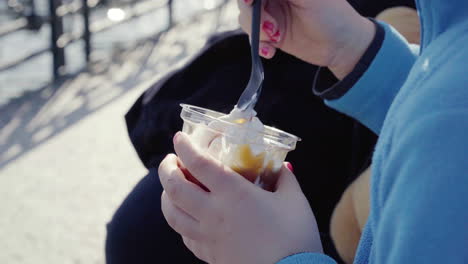 Close-up-of-little-girl-with-blue-jumper-nail-polish-and-teddy-bear-beside-her-holding-a-sundae-ice-cream-sitting-outdoor-4k