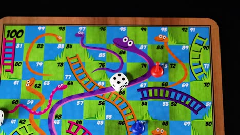a hand moves pieces and rolls dice on a vibrant board with snakes and ladders.