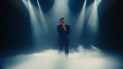 man singing on stage with spotlights and smoke