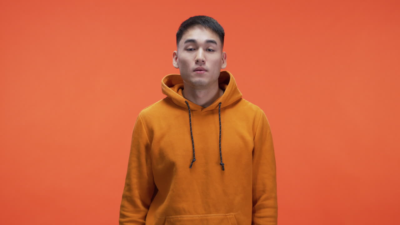 Man in orange hoodie covering his ears
